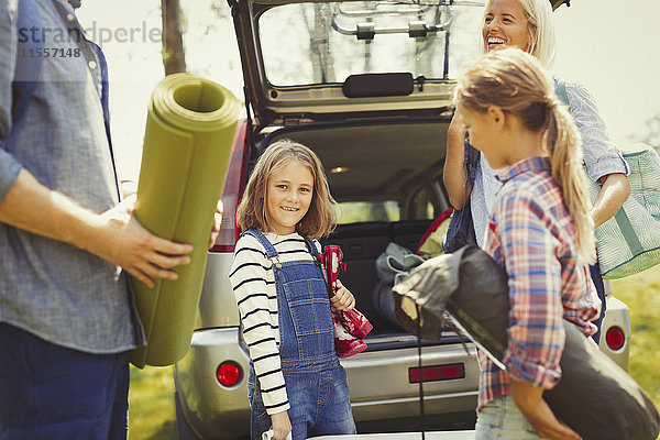 Portrait lächelndes Mädchen mit Familie beim Entladen der Campingausrüstung aus dem Auto