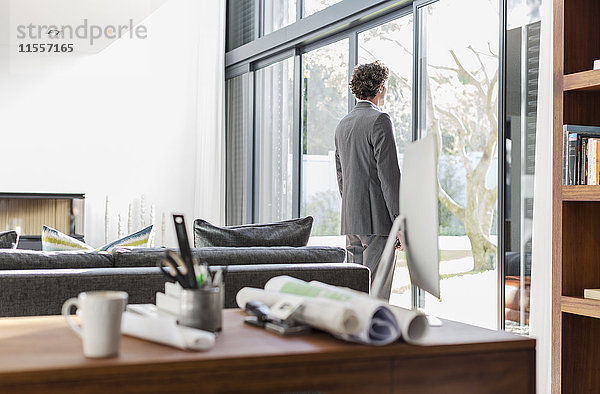 Männlicher Architekt schaut aus dem Terrassenfenster im Büro zu Hause