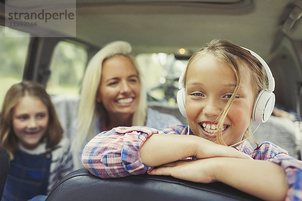 Portrait lächelndes Mädchen mit Kopfhörer auf dem Rücksitz des Autos