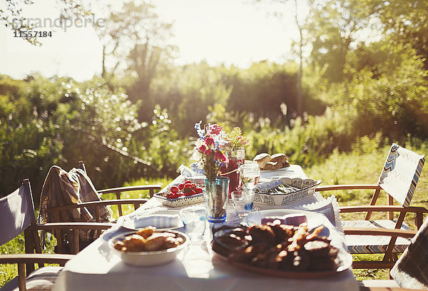 Essen und Blumenstrauß auf sonnigem Gartenparty-Tisch