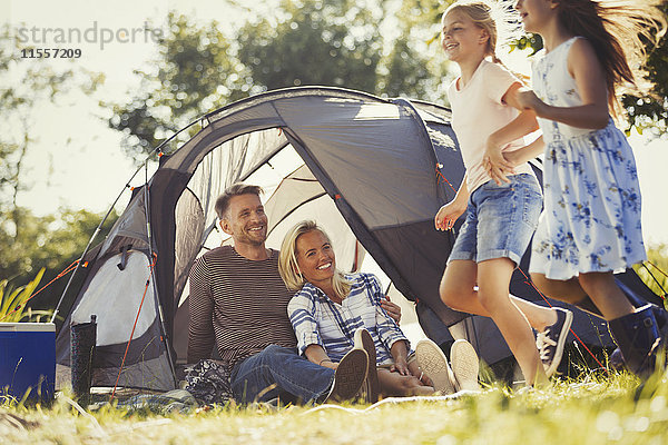 Eltern beobachten glückliche Töchter  die im sonnigen Zelt des Campingplatzes herumlaufen.