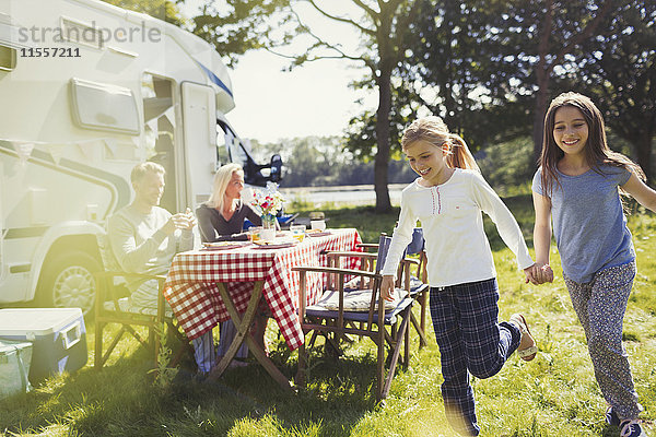 Glückliche Schwestern halten sich an den Händen und laufen im sonnigen Wohnmobil herum.