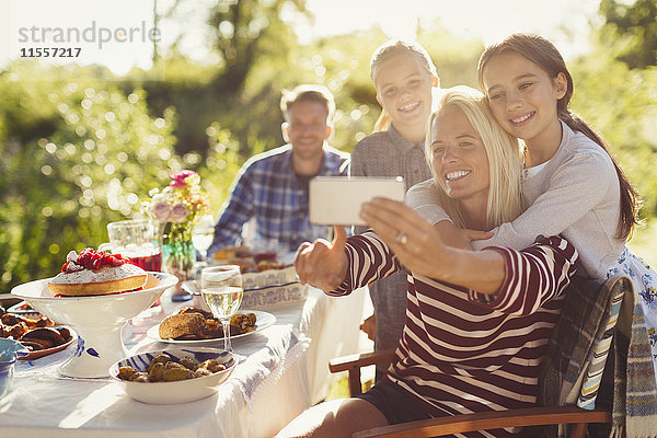 Mutter und Töchter  die Selfie mit Fotohandy am Gartenparty-Tisch nehmen