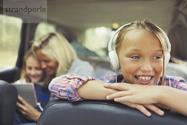 Lächelndes Mädchen hört Musik mit Kopfhörern auf dem Rücksitz des Autos.