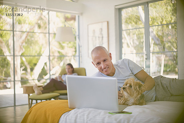 Lächelnder Mann mit Hund am Laptop auf dem Bett