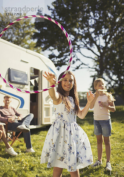 Portrait Verspieltes Mädchen beim Spinnen von Plastikreifen vor dem sonnigen Wohnmobil