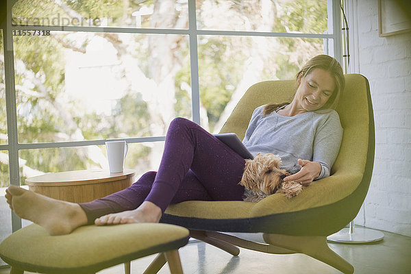 Frau mit Laptop entspannt und streichelt Hund auf Stuhl