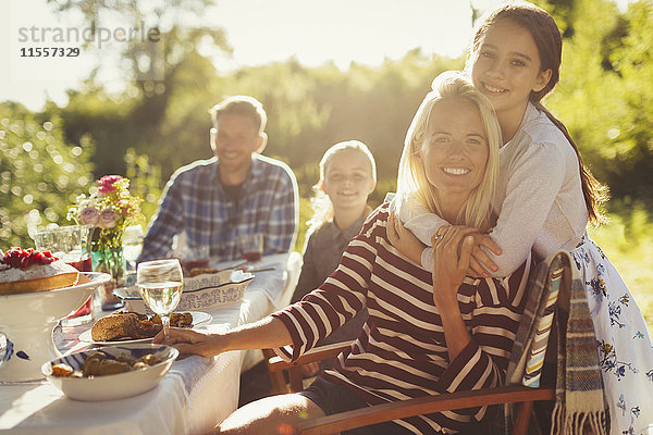 Portrait lächelnd liebevolle Mutter und Tochter umarmend am sonnigen Gartenparty-Tisch