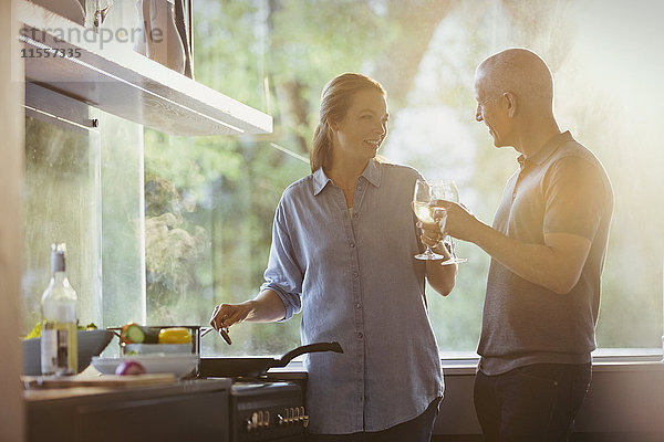 Ehepaar stößt mit Weißweingläsern an und kocht in der Küche