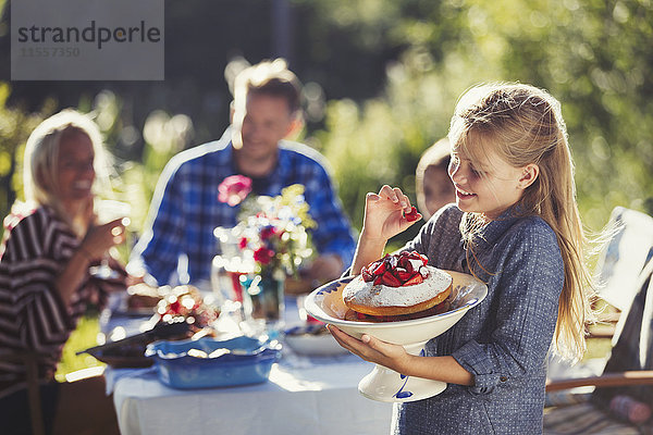 Mädchen mit Erdbeerkuchen am sonnigen Gartenparty-Tisch