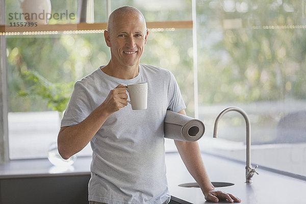 Portrait lächelnder reifer Mann mit Yogamatte trinkt Kaffee in der Küche