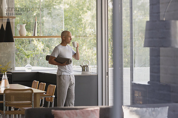 Älterer Mann mit Yogamatte trinkt Kaffee in der Küche