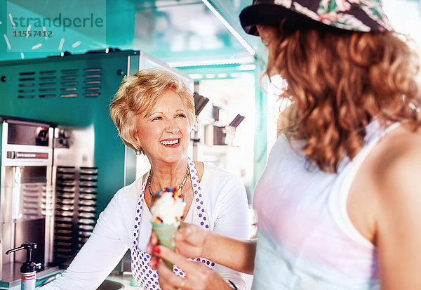 Lächelnde Seniorin  die der jungen Frau im Speisewagen Eis serviert.