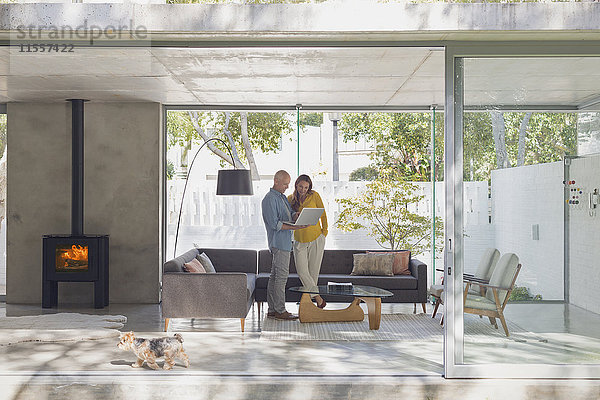 Ein Paar benutzt einen Laptop in einem modernen Wohnzimmer mit Blick auf den Innenhof