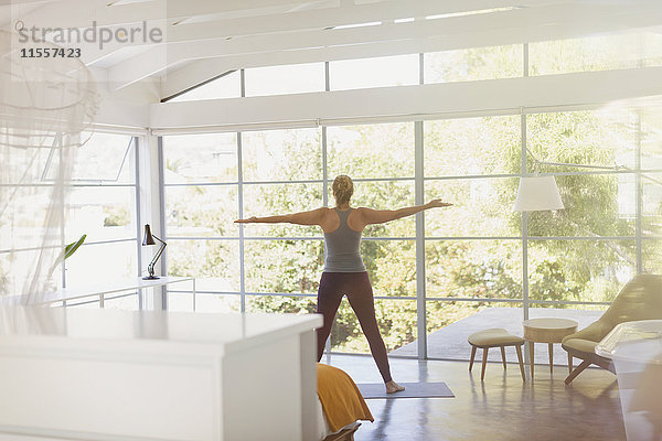 Frau übt Yoga mit ausgestreckten Armen in einem sonnigen modernen Schlafzimmer