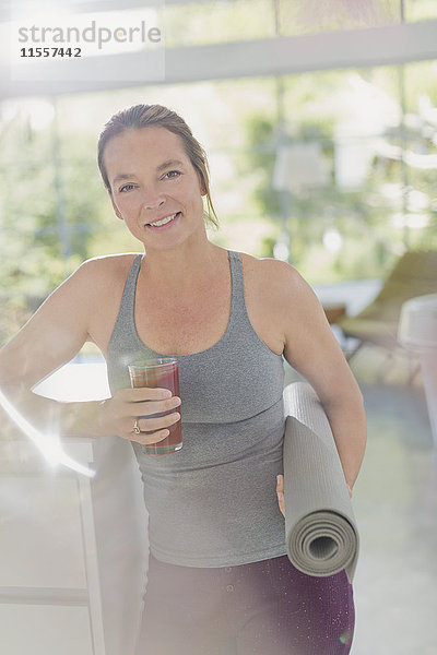 Porträt lächelnde reife Frau mit Yogamatte trinkt Saft Smoothie