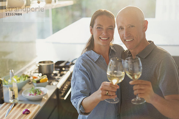 Porträt glückliches reifes Paar  das mit Weißweingläsern anstößt und in der Küche kocht