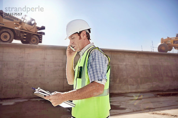 Bauarbeiter-Vorarbeiter im Gespräch am Handy auf der sonnigen Baustelle