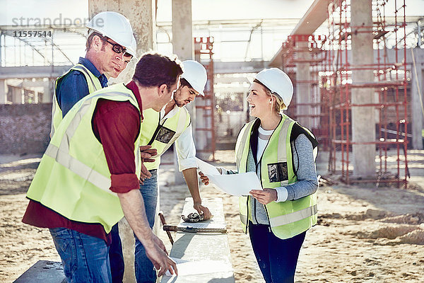 Vorarbeiterinnen im Gespräch mit Bauarbeitern auf der sonnigen Baustelle
