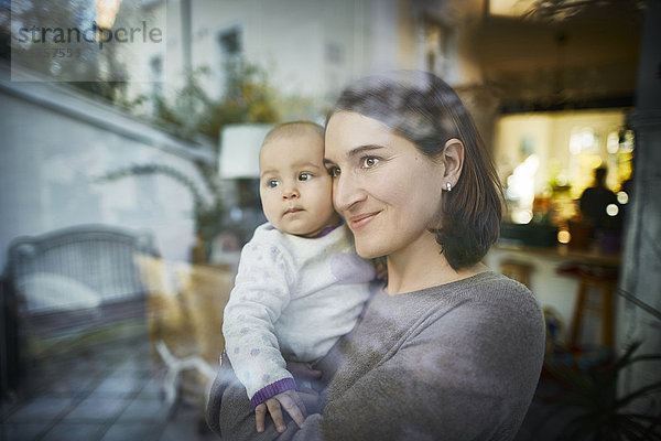 Lächelnde Mutter hält Baby-Tochter am Fenster