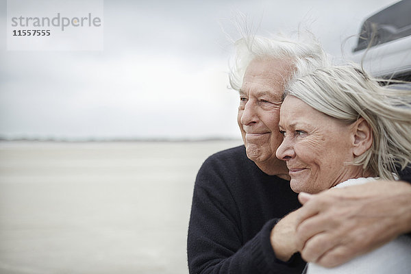 Zärtliches Seniorenpaar  das sich am Strand umarmt und wegschaut.