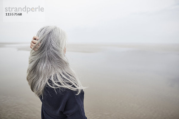 Seniorin mit Hand in langen grauen Haaren am Winterstrand