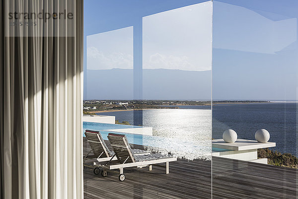 Blick aus dem Fenster auf die sonnige  moderne und luxuriöse Terrasse mit Infinity-Pool und Meerblick
