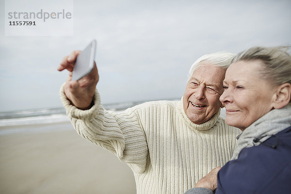 Senior Paar nimmt Selfie mit Handy am windigen Winterstrand