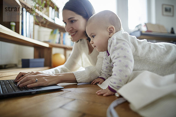 Baby Tochter beobachtet Mutter beim Tippen auf dem Laptop auf dem Boden
