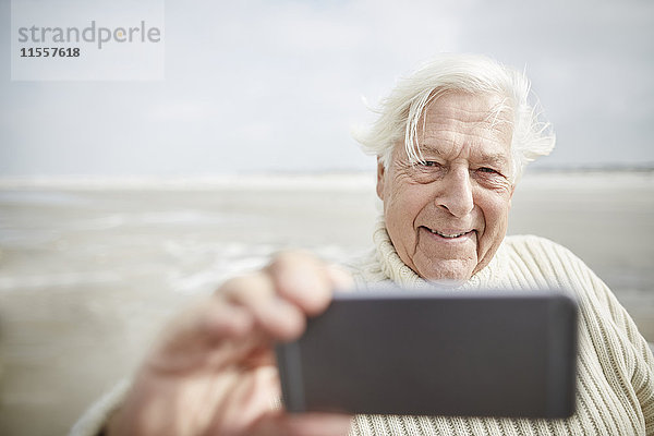 Lächelnder älterer Mann  der Selfie mit Handy am Strand nimmt