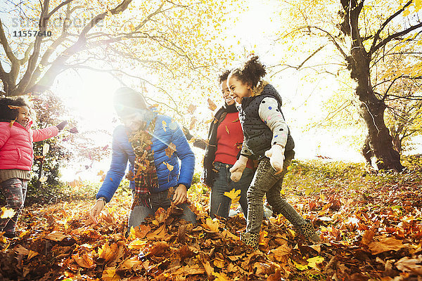 Verspielte junge Familie beim Spielen im Herbstlaub im sonnigen Park