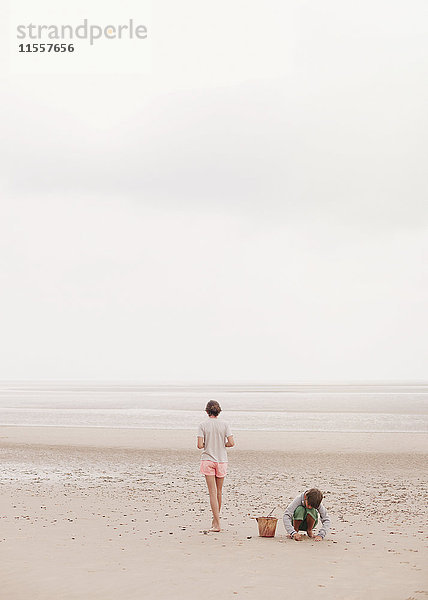 Bruder und Schwester spielen im Sand am bedeckten Sommerstrand