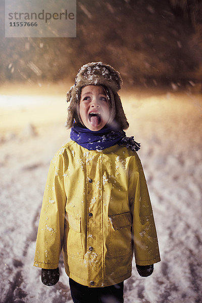 Junge in warmer Kleidung streckt die Zunge heraus und probiert Schnee