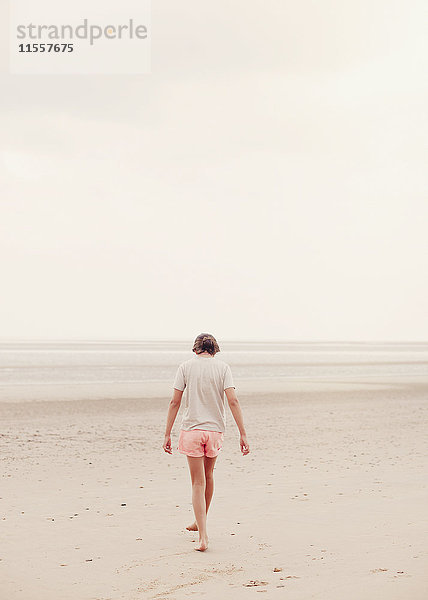 Teenager-Mädchen  das an einem bedeckten Sommerstrand im Sand spazieren geht