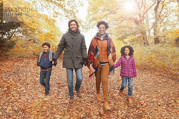 Porträt einer lächelnden jungen Familie  die sich an den Händen hält und den Weg im Herbstpark geht.