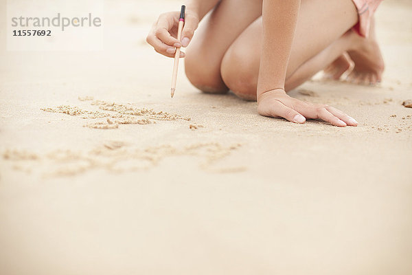 Mädchen mit Bleistift schreibt im Sand am Sommerstrand