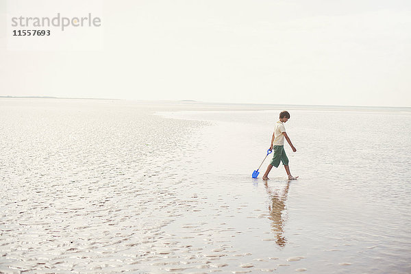 Junge geht mit Schaufel in nassem Sand an einem bewölkten Sommerstrand