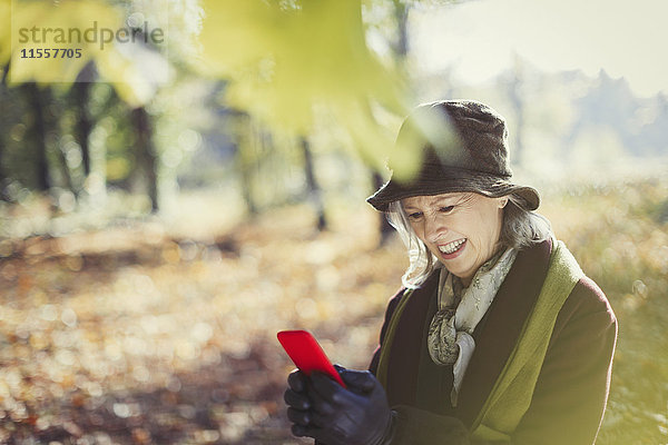 Lächelnde Seniorin mit Handy im sonnigen Herbstpark