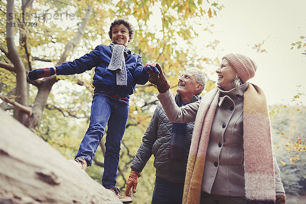 Großeltern gehender Enkel auf Baumstamm im Herbstpark