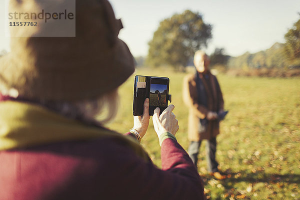 Seniorin mit Fotohandy fotografiert Ehemann im sonnigen Herbstpark