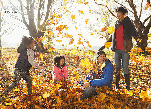 Junge Familie spielt im Herbstlaub im sonnigen Park