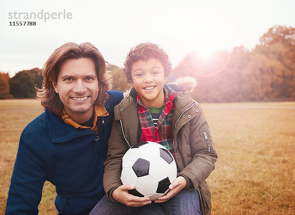 Portrait lächelnder Vater und Sohn mit Fußball im Parkgras