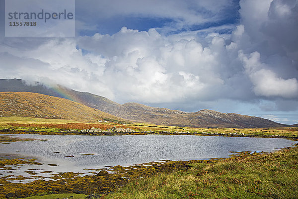 Ruhiger Blick auf Wolken und Regenbogen über sanfte Hügel jenseits des Sees  Loch Aineort  South Uist  Outer Hebrides