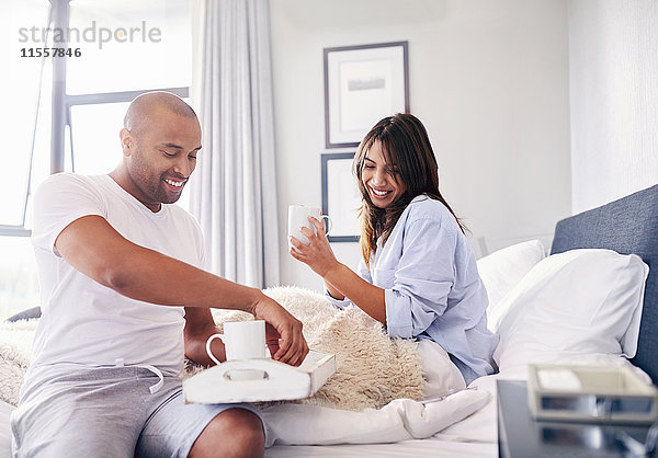 Lächelndes Paar trinkt Kaffee im Bett