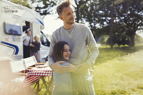 Zärtliche Umarmung von Vater und Tochter vor dem sonnigen Wohnmobil