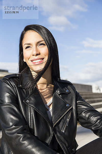 Porträt einer lächelnden jungen Frau mit Nasenpiercing in schwarzer Lederjacke