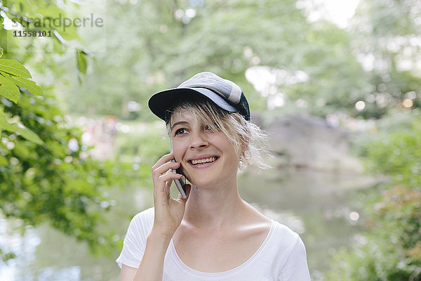 Lächelnde junge Frau im Park spricht am Handy