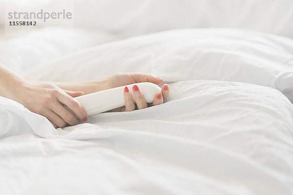 Hand der Frau mit Sexspielzeug im Bett