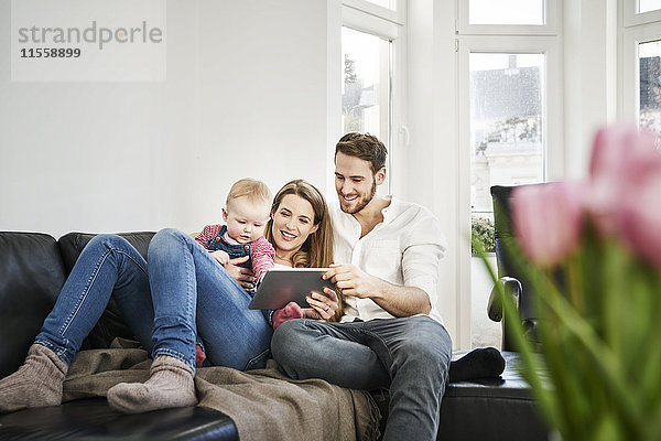 Eltern mit Baby-Mädchen beim Betrachten der Tablette auf der Couch