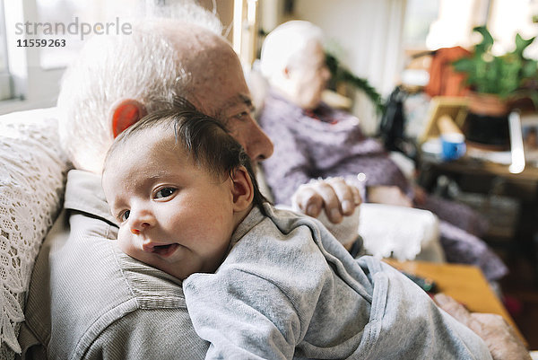 Urgroßvater hält Baby zu Hause mit seiner Frau im Hintergrund